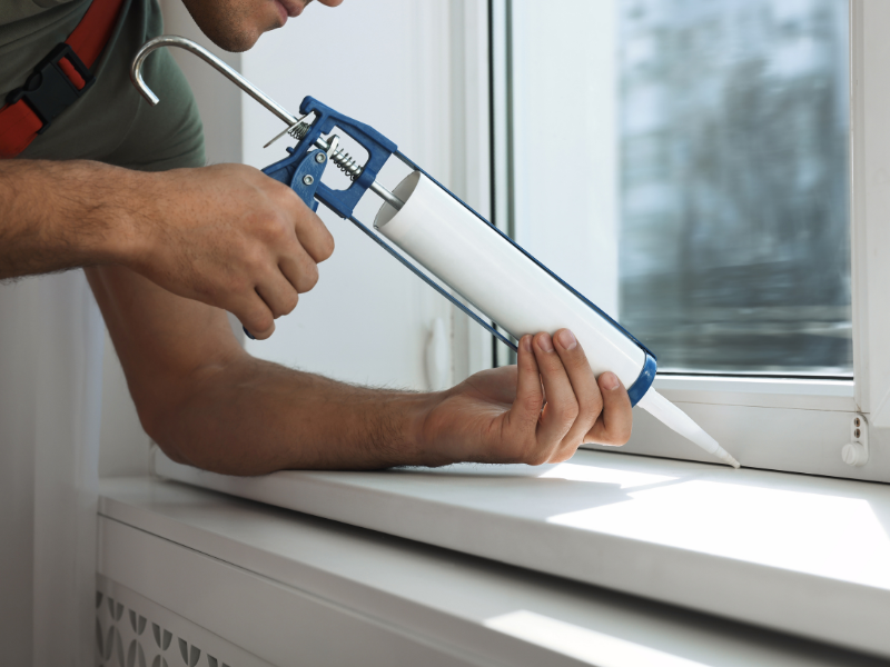 A person sealing cracks around a window.