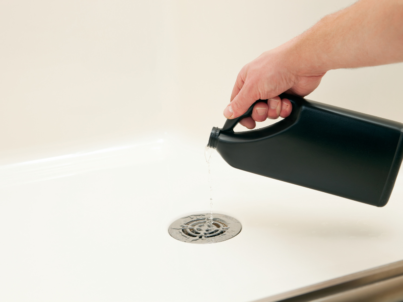 Chemical drain cleaner bottle pouring into a clogged sink.